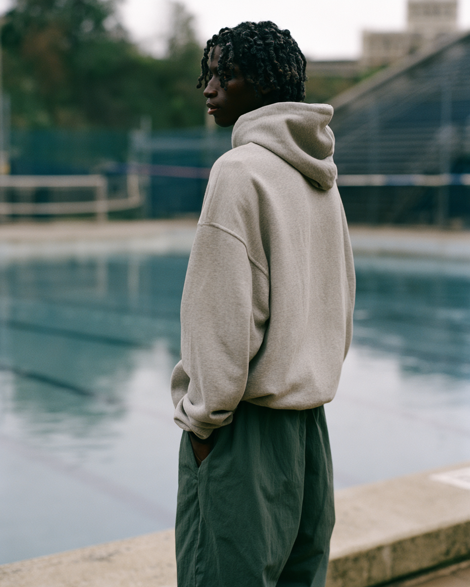 Model at the edge of the empty campus pool in the practice hoodie and track pants